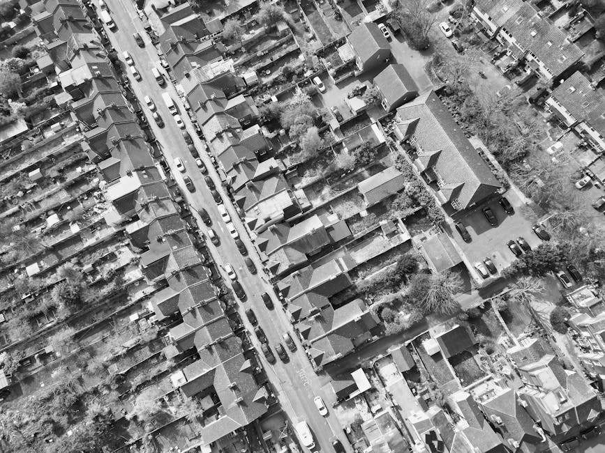 An aerial black and white photograph of a densely populated suburban neighborhood showing tightly packed terraced houses with pitched roofs, small gardens, and narrow alleyways. The houses are aligned