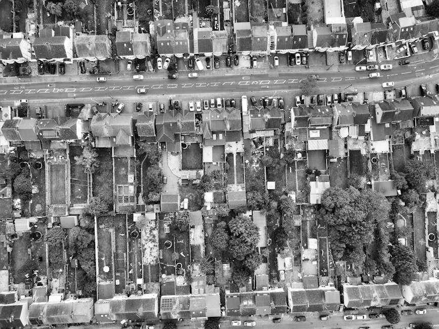 An aerial black and white photograph of a densely populated suburban neighborhood showing tightly packed terraced houses with pitched roofs, small gardens, and narrow alleyways. The houses are aligned
